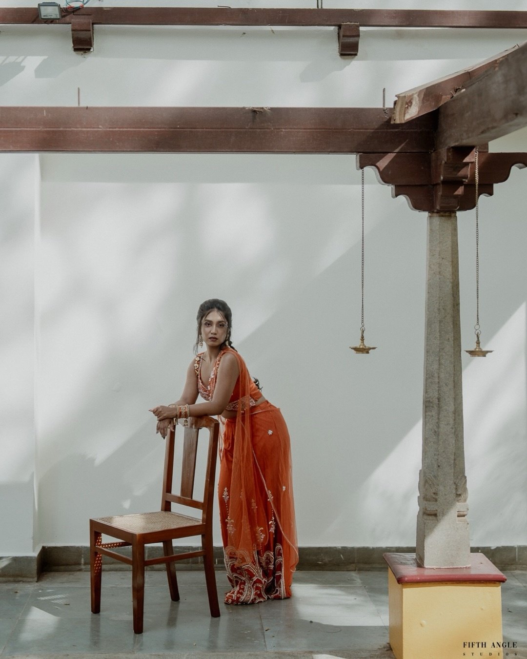 A bride posing beside a chair in a sunlit heritage courtyard